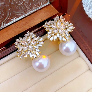 Detail of flower-shaped earrings with crystals and hanging pearl on beige velvet tray