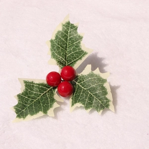 Künstliche Weihnachts-Stechpalmenblätter mit roten Beeren auf weißem Plüsch