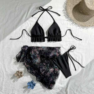 Flat lay of black three-piece bikini set with floral mesh skirt and beach accessories