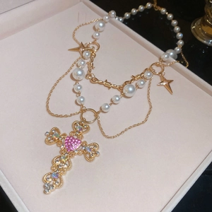 Detail of layered pearl necklace with gold cross pendant and pink heart gemstone