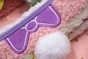 Macro detail of plush pink pencil case with purple bow embroidery and soft textures