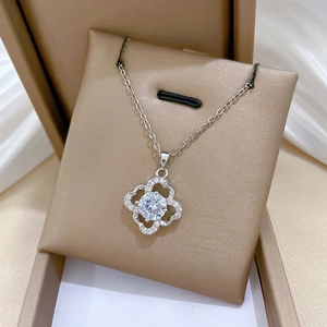 Macro shot of silver clover pendant with central crystal on beige jewelry cushion