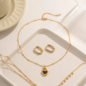 Detail of 18K gold stainless steel necklace with black heart pendant and earrings on a tray