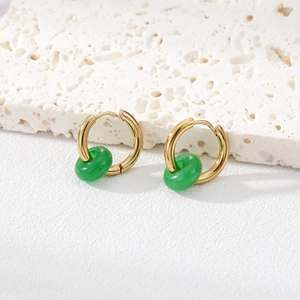 Gold hoop earrings with a green round natural stone pendant on a white travertine block