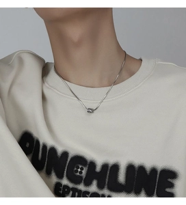 Close-up of checkered cylindrical pendant on silver snake chain worn by male model