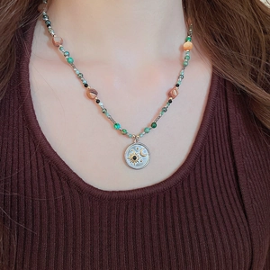 Détail du collier de perles avec pendentif céleste porté sur un pull en maille marron