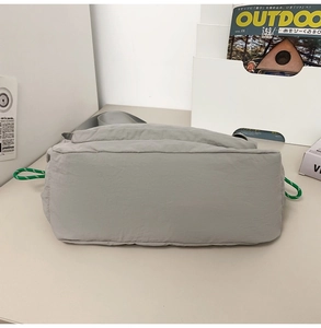 Base view of gray nylon messenger bag with reinforced stitching and green cord details