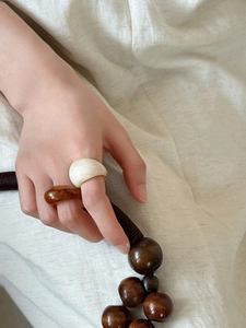 Detail of cream and amber brown resin rings worn on fingers with soft fabric background