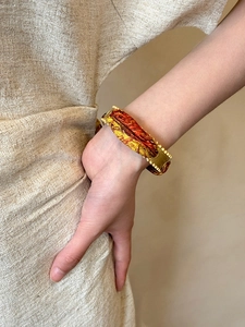 Detail of vintage matte gold open cuff bracelet with orange silk wrap on model's wrist