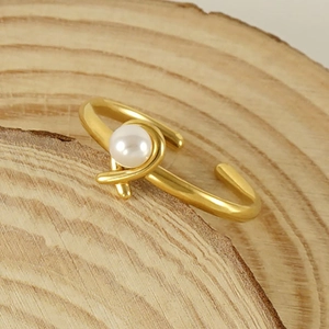 Adjustable golden stainless steel open ring with a single white pearl on wood block