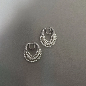 Detail of silver multi-layer pearl earrings with zircon horseshoe clasp on textured surface