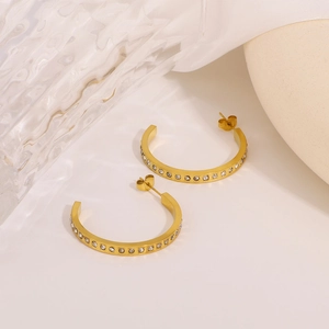 Boucles d'oreilles dorées en C avec strass brillants sur un fond blanc épuré