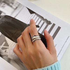 Close-up of a double-layered wavy sterling silver ring worn on a hand over a fashion magazine