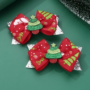 Detail of red Christmas hair bows with glittery green trees on a dark pine background