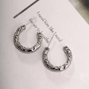 Detailed macro view of irregular C-shaped silver earrings with hammered metal texture
