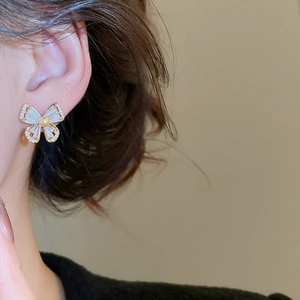 Close-up of golden butterfly earring with cubic zirconia and pearl on ear