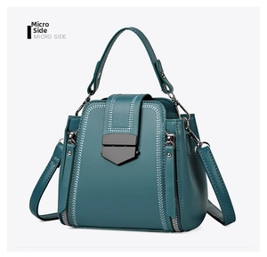 Detail view of dark green textured leather bag with white chevron stitching and metal lock