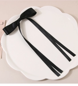 Detail of a large black ribbon bow hair clip with long streamers on a white decorative tray
