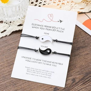 Handmade Yin Yang braided bracelets for couples on message card over wooden surface
