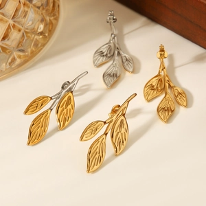 Detailed view of gold and silver leaf-shaped stainless steel earrings on a beige surface