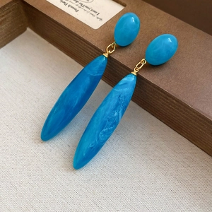 Detailed macro view of bright blue marble-textured acrylic waterdrop earrings on fabric