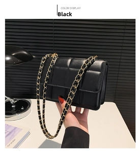 Detail of black quilted leather shoulder bag with gold chain strap in home setting