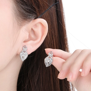 Close-up of minimalist heart-shaped silver earrings with sparkling stones on model ear