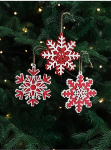 Close-up of red and white wooden snowflake ornaments hanging on a lit Christmas tree