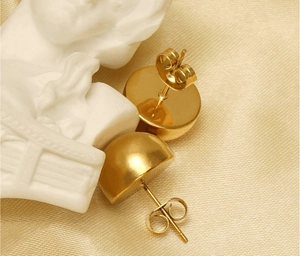 Detailed close-up of golden hemisphere stud earrings on elegant silk fabric background