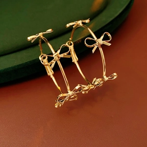 Detailed view of large gold hoop earrings with delicate multiple bow accents on dark surface