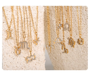 Detailed view of gold-plated zodiac pendants with sparkling crystal inlay on stone surface