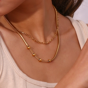 Detail of layered gold snake chain and round bead necklace on female model neck
