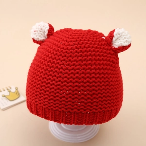 Detailed view of handmade red knit baby hat with cute bicolor pom-pom ears