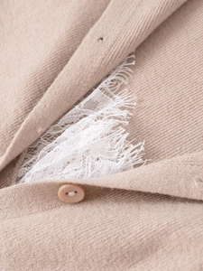 Macro view of light khaki knit fabric featuring white eyelash lace and resin button