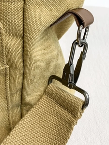 Close-up of khaki canvas messenger bag featuring durable metal hooks and leather accents