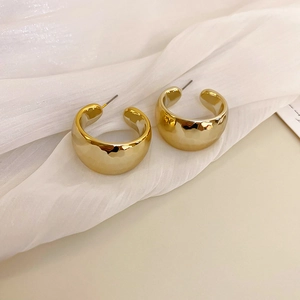 Macro shot of thick gold C-shaped hoop earrings with polished finish on white fabric
