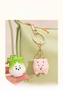 Detailed view of cute pig and cabbage silicone charms on a textured green leather handbag