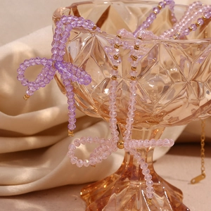 Detail of beaded necklace with purple crystals and gold bow on amber glass