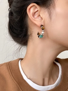 Close-up of a model wearing C-shaped earrings with cat-eye and tiger-eye stone beads