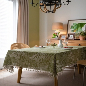 Detail of green linen tablecloth featuring white botanical patterns and decorative fringe