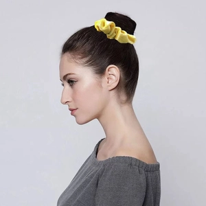 Elastic velvet scrunchie in bright yellow color styled on a woman's hair bun