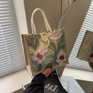 Detailed embroidery of white flowers and green leaves on a linen handbag with rope handles