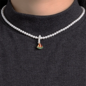 Detail view of a pearl necklace with a gold-rimmed watermelon pendant on a model