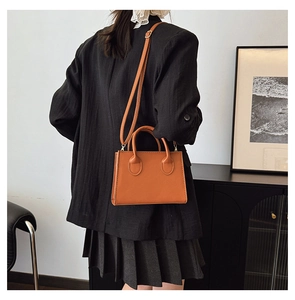 Brown leather-like handbag shown on a model with dual handles and adjustable shoulder strap