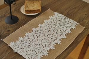 Close-up of linen placemat with white floral lace trim on a dark wood table