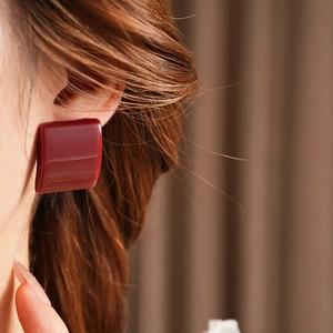 Primo piano di eleganti orecchini quadrati in resina bordeaux indossati da una modella