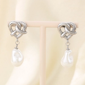 Detailed view of silver heart knot earrings with baroque pearl drops on a T-bar stand