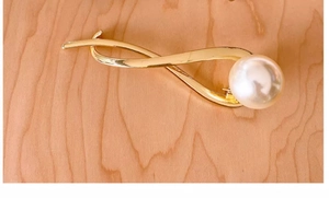 Detailed close-up of a gold metal twisted hair clip with a large pearl on wood surface
