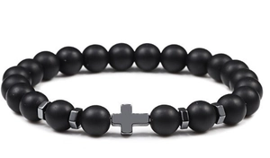 Detail of matte black beaded bracelet featuring a metallic cross charm on white background
