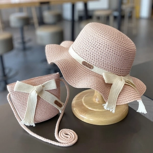 Detail of pink straw sun hat and matching bag set with woven bows on a wooden stand